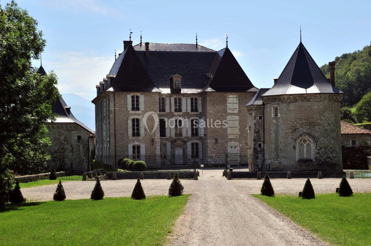 Château historique en pierre entouré de tours, situé au bout d'une allée bordée de pelouses et d'arbres.