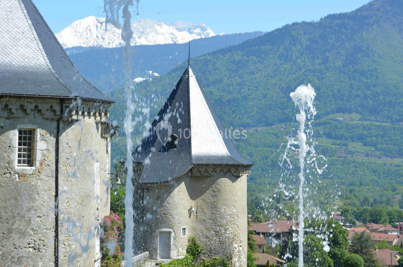 Fontaines jaillissantes devant des bâtiments historiques avec des montagnes enneigées en arrière-plan.