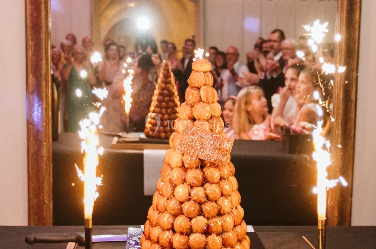 Pièce montée en choux décorée de cierges magiques allumés, entourée d'invités lors d'une célébration.