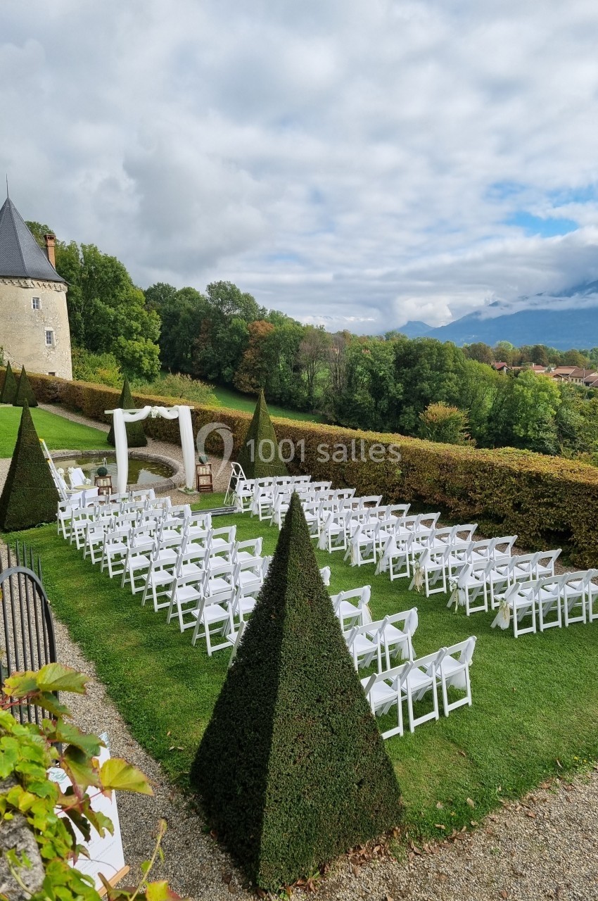 Chaises blanches alignées en extérieur pour une cérémonie, avec une arche décorée et un château en arrière-plan.