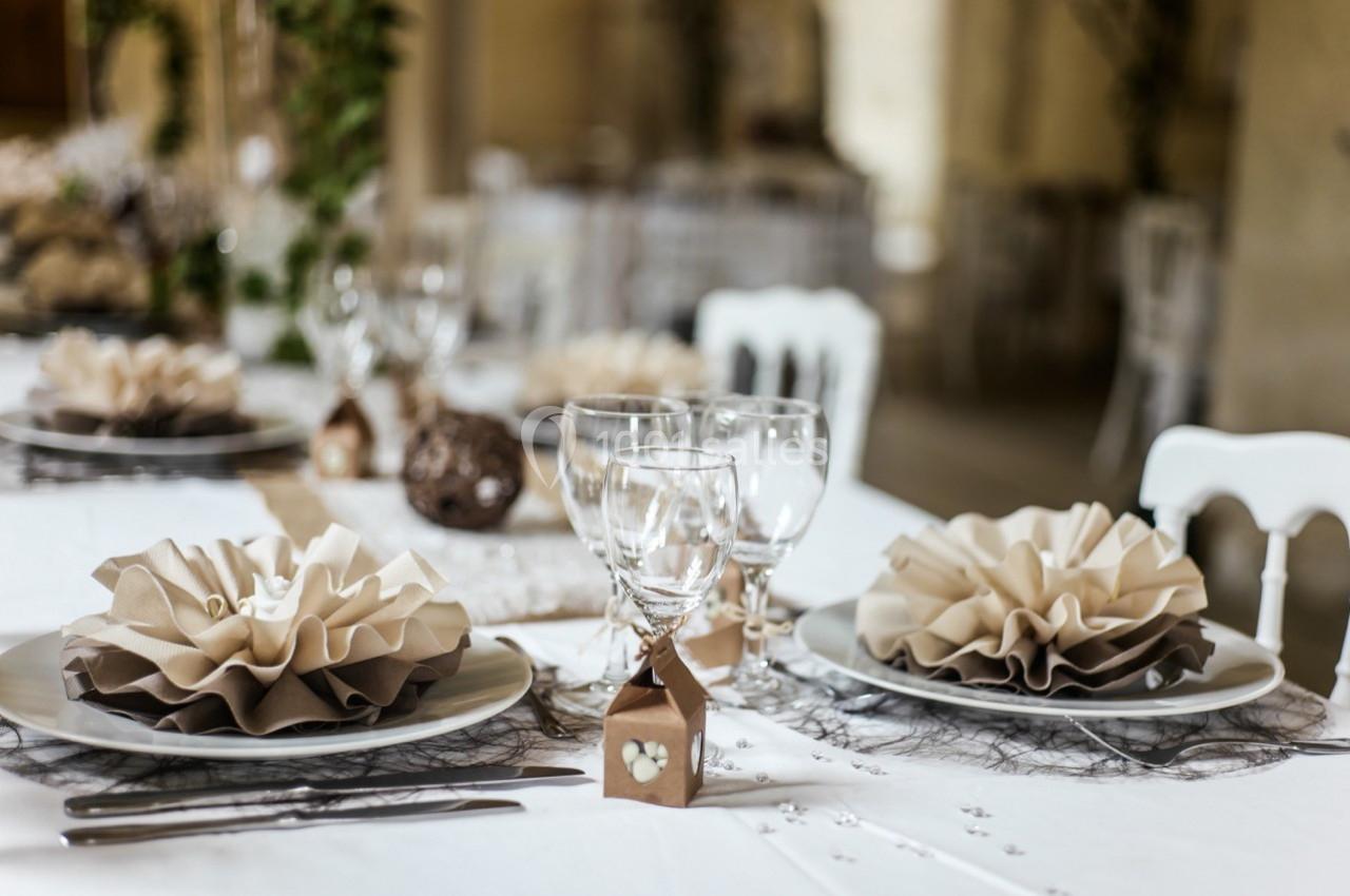 Table élégamment dressée avec assiettes, serviettes pliées en éventail, verres à pied et décorations raffinées.