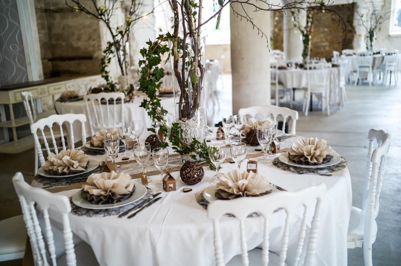 Table décorée pour un événement, avec nappes blanches, pliages de serviettes en forme de fleurs et centre de table végétal.