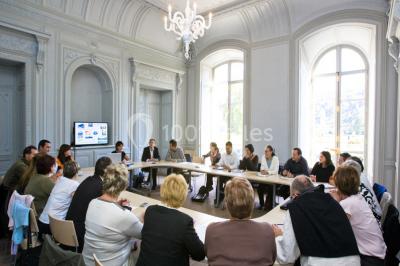 Salle voûtée élégamment dressée pour un repas, avec tables ornées de nappes blanches, verres et assiettes décorées.