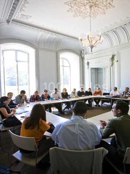Des personnes assises autour d'une grande table dans une salle lumineuse avec des moulures au plafond.