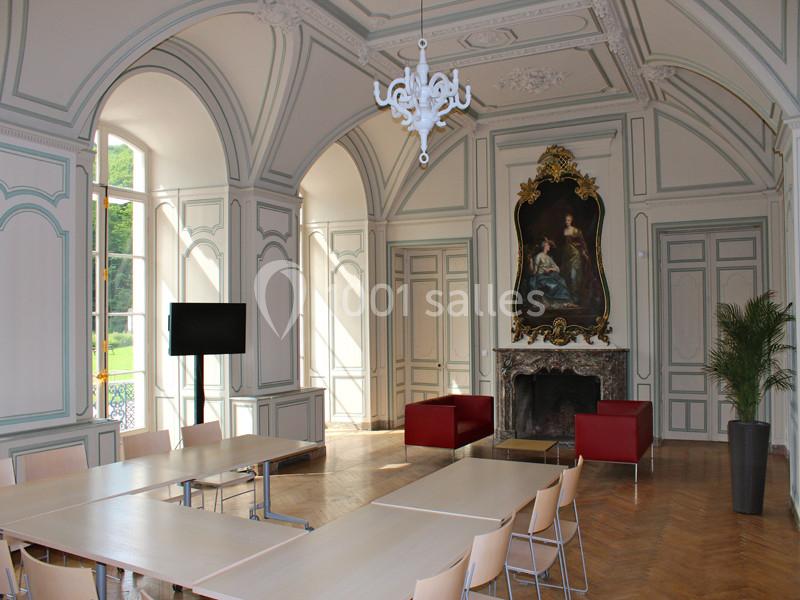 Salle lumineuse avec murs ornés, cheminée, tableau, mobilier moderne et grandes fenêtres donnant sur un jardin.