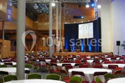 Salle voûtée élégamment dressée pour un repas, avec tables ornées de nappes blanches, verres et assiettes décorées.