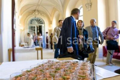 Salle voûtée élégamment dressée pour un repas, avec tables ornées de nappes blanches, verres et assiettes décorées.