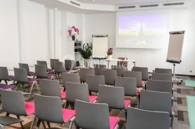 Salle de réunion aménagée en U avec tables, chaises colorées, écran, paperboard et bouteilles d'eau.