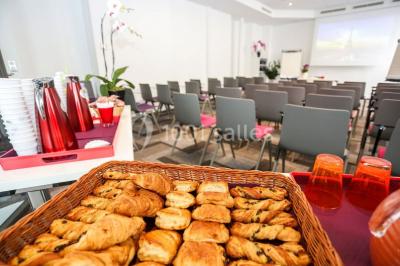 Salle de réunion aménagée en U avec tables, chaises colorées, écran, paperboard et bouteilles d'eau.