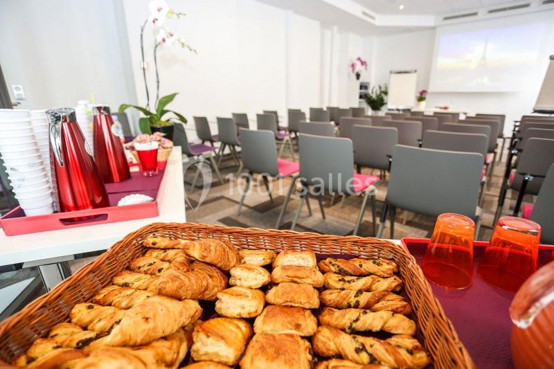 Panier de viennoiseries au premier plan dans une salle de réunion équipée de chaises et d'un écran de projection.