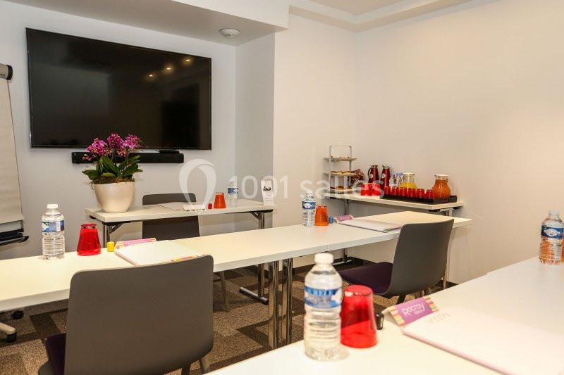 Salle de réunion équipée avec tables, chaises, écran, fleurs, bouteilles d'eau et collations sur une table d'appoint.