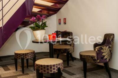 Salle de réunion aménagée en U avec tables, chaises colorées, écran, paperboard et bouteilles d'eau.