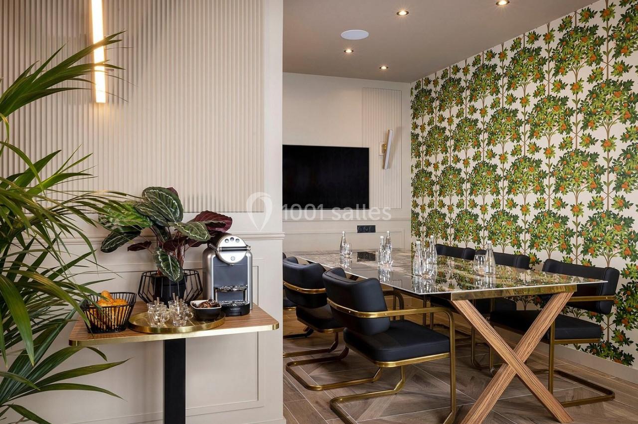 Salle à manger moderne avec table en verre, chaises noires, mur à motif floral et coin café avec machine à expresso.