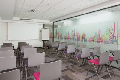 Salle de réunion aménagée en U avec tables, chaises colorées, écran, paperboard et bouteilles d'eau.