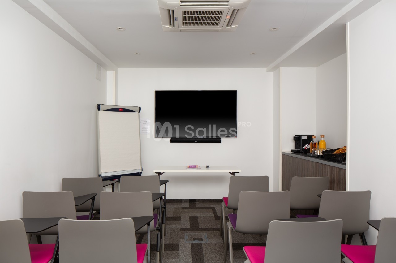 Salle de réunion équipée de chaises, écran mural, paperboard et coin rafraîchissements avec boissons et collations.