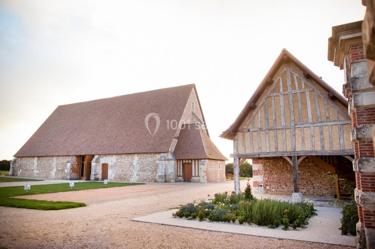 Deux bâtiments anciens à colombages et en pierre, entourés d'une cour gravillonnée et d'espaces verts.
