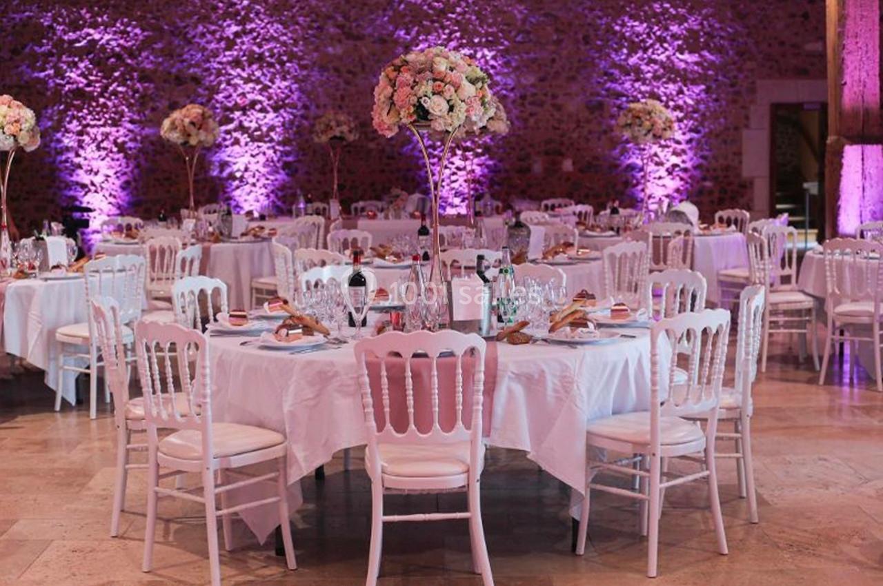 Salle de réception décorée avec des tables rondes, nappes blanches, chaises assorties et centres de table fleuris.