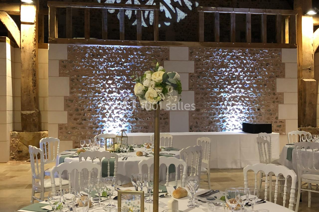 Salle de réception décorée avec des tables élégantes, nappes blanches, centres de table fleuris et éclairage chaleureux.