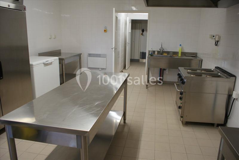 Cuisine professionnelle avec plans de travail en inox, cuisinière, évier et murs carrelés blancs.