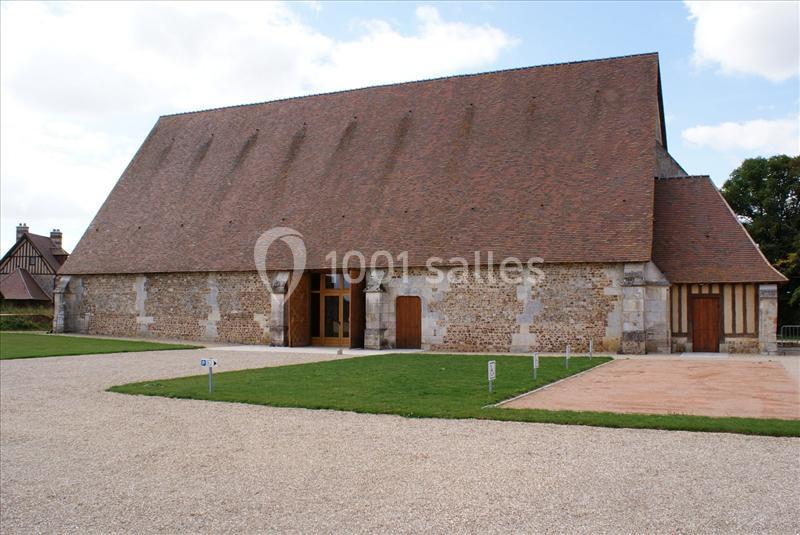 Bâtiment en pierre avec un toit en tuiles rouges, entouré d'une cour en gravier et d'espaces verts.