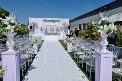 Salle de réception élégante avec tables décorées de fleurs blanches, chaises transparentes et éclairage tamisé.