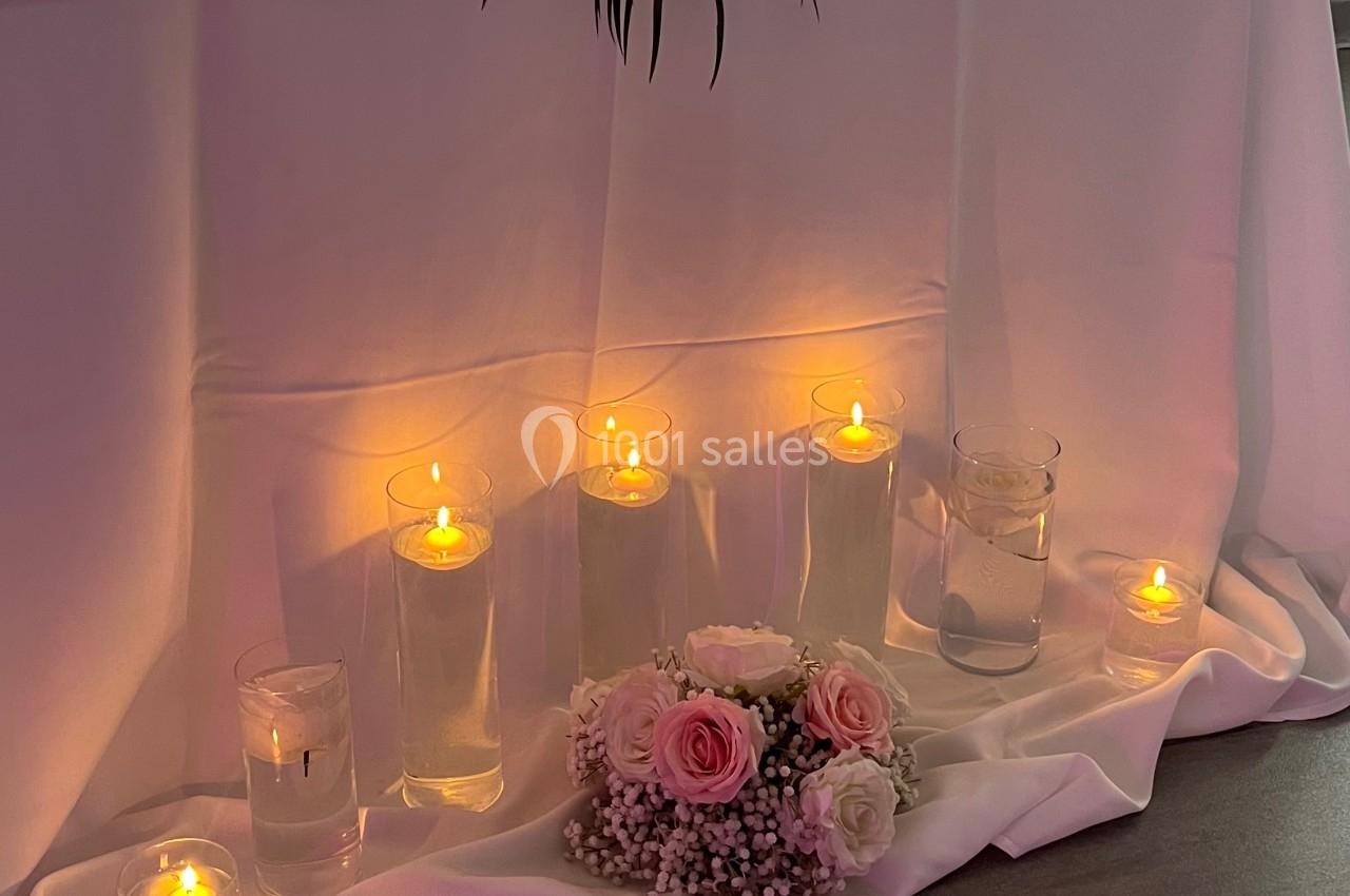 Table décorée pour un événement avec fleurs roses et blanches, bougies allumées et voilage en arrière-plan.