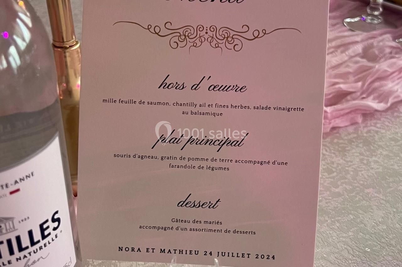 Carte de menu de mariage posée sur une table décorée avec des bougies, nappes blanches et éléments roses.