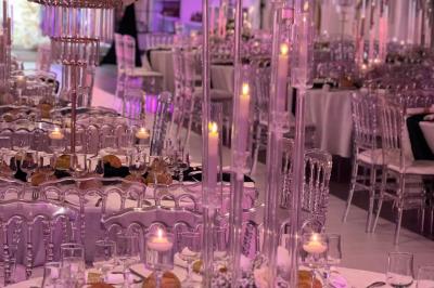 Salle de réception élégante avec tables décorées de fleurs blanches, chaises transparentes et éclairage tamisé.