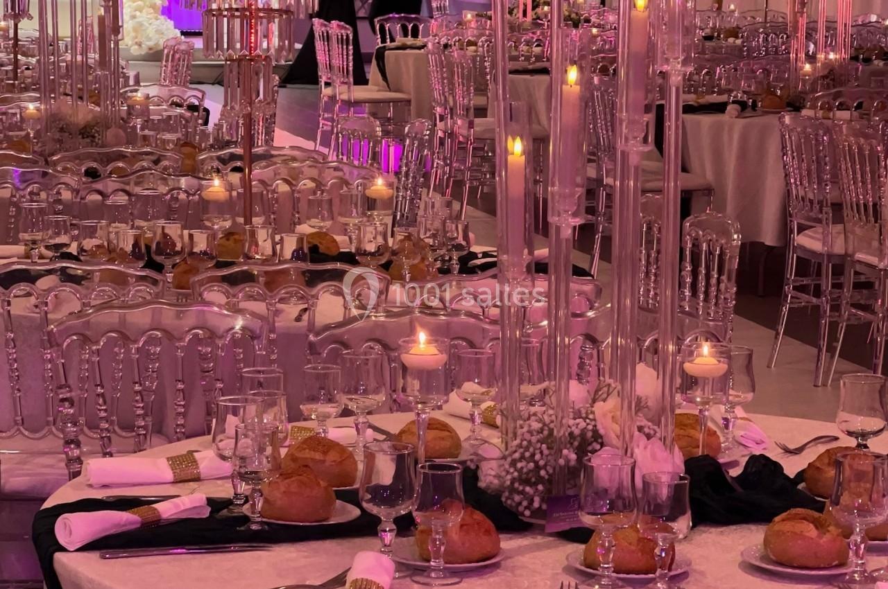 Salle de réception élégamment décorée avec tables dressées, chandeliers, fleurs blanches et éclairage tamisé.