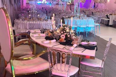 Salle de réception élégante avec tables décorées de fleurs blanches, chaises transparentes et éclairage tamisé.