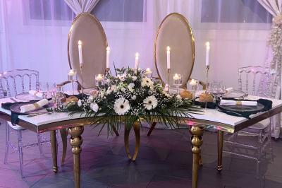 Salle de réception élégante avec tables décorées de fleurs blanches, chaises transparentes et éclairage tamisé.