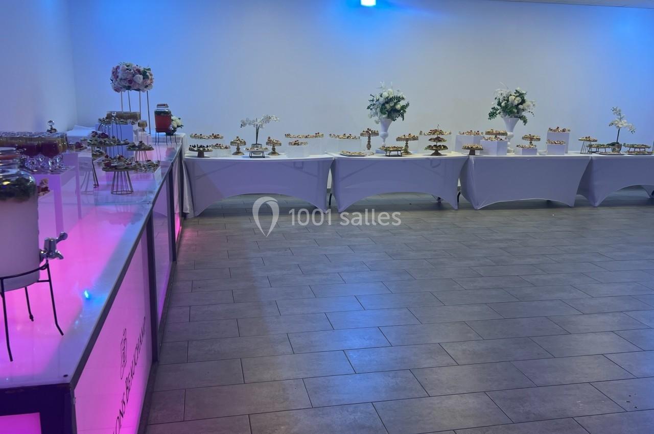 Buffet de desserts variés disposés sur des tables blanches dans une salle éclairée par des lumières colorées.