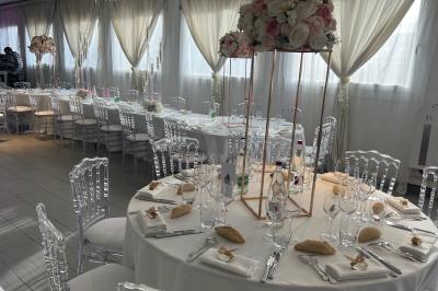 Salle de réception élégante avec tables décorées de fleurs blanches, chaises transparentes et éclairage tamisé.