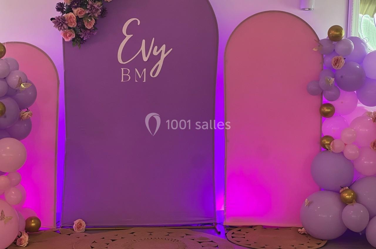 Mur décoratif avec panneaux roses et violets, ballons assortis et fleurs, utilisé pour un événement festif.