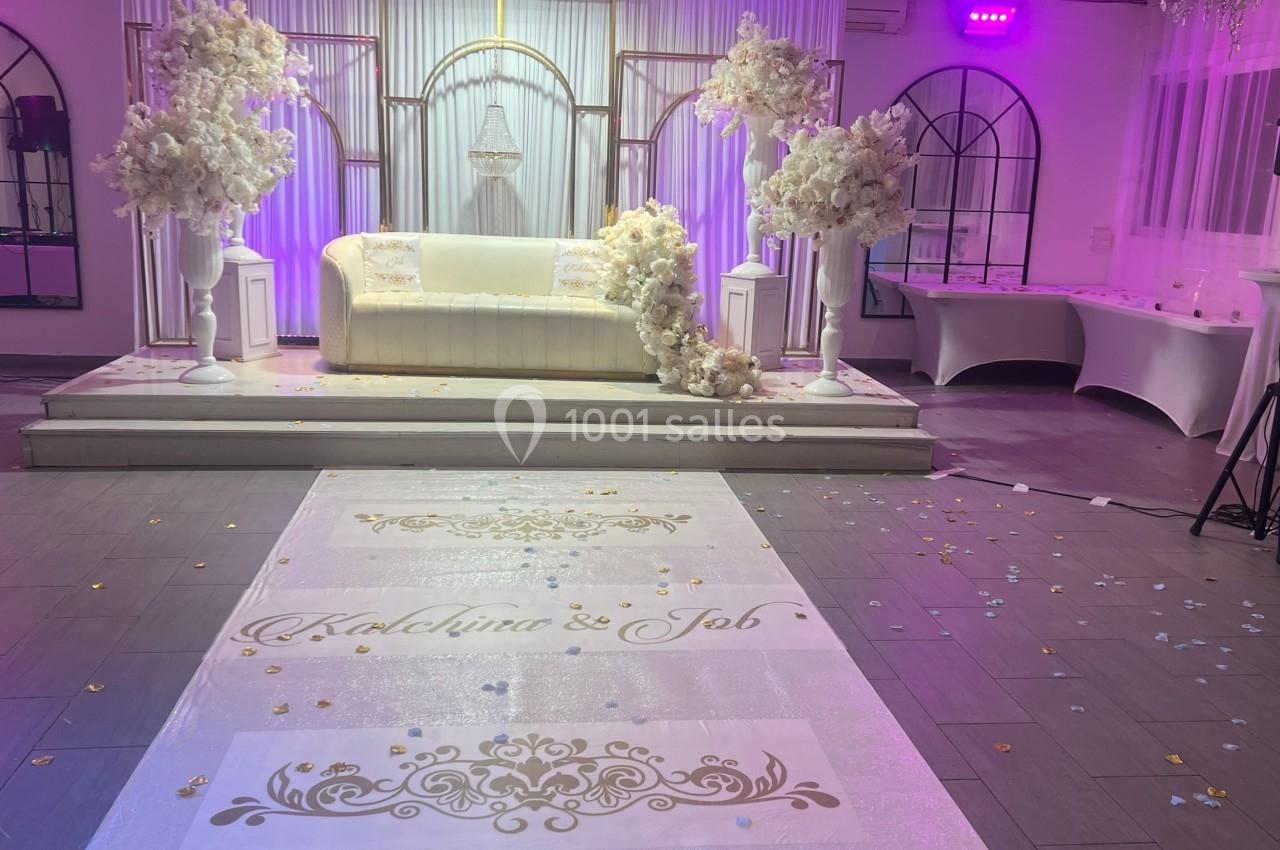 Salle de réception décorée pour un mariage, avec un canapé blanc, des fleurs blanches et une allée personnalisée.