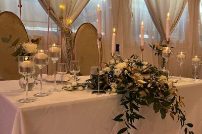 Salle de réception élégante avec tables décorées de fleurs blanches, chaises transparentes et éclairage tamisé.