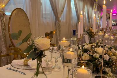 Salle de réception élégante avec tables décorées de fleurs blanches, chaises transparentes et éclairage tamisé.