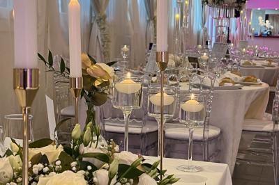 Salle de réception élégante avec tables décorées de fleurs blanches, chaises transparentes et éclairage tamisé.