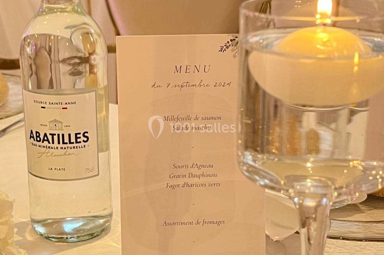 Bouteille d'eau, menu imprimé et bougie sur une table élégamment dressée pour un repas.