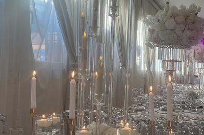 Salle de réception élégante avec tables décorées de fleurs blanches, chaises transparentes et éclairage tamisé.