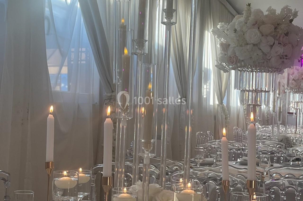 Bougies allumées et décorations florales blanches sur une table élégamment dressée dans une salle lumineuse.