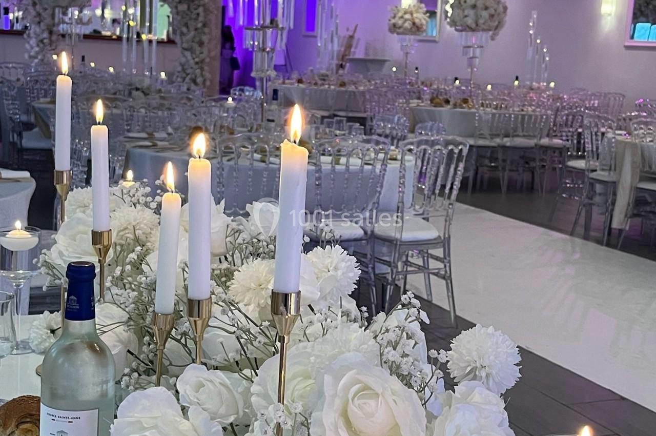 Salle de réception élégante décorée de fleurs blanches, chandeliers et bougies allumées sur des tables dressées.