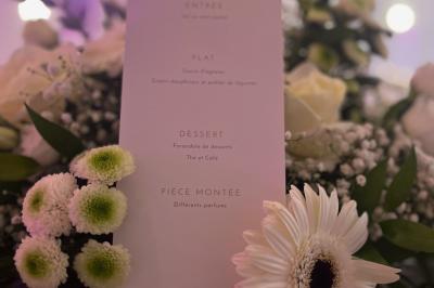 Salle de réception élégante avec tables décorées de fleurs blanches, chaises transparentes et éclairage tamisé.
