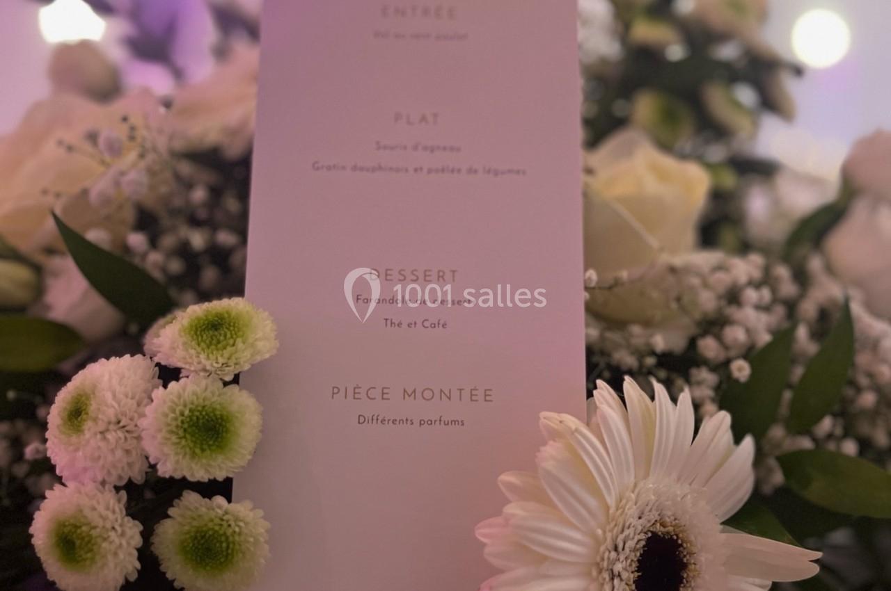 Menu imprimé sur une carte blanche entourée de fleurs blanches et vertes dans un décor lumineux.