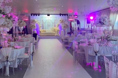 Salle de réception élégante avec tables décorées de fleurs blanches, chaises transparentes et éclairage tamisé.