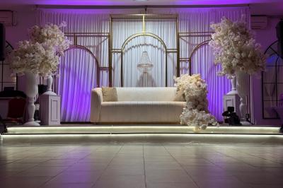 Salle de réception élégante avec tables décorées de fleurs blanches, chaises transparentes et éclairage tamisé.