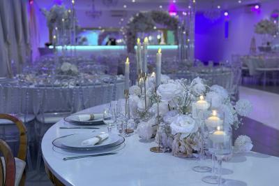 Salle de réception élégante avec tables décorées de fleurs blanches, chaises transparentes et éclairage tamisé.