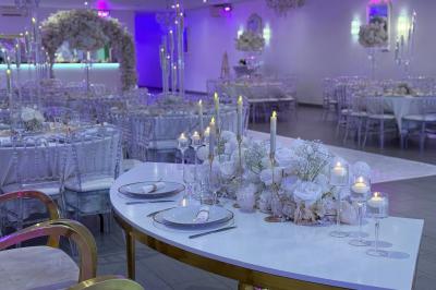 Salle de réception élégante avec tables décorées de fleurs blanches, chaises transparentes et éclairage tamisé.