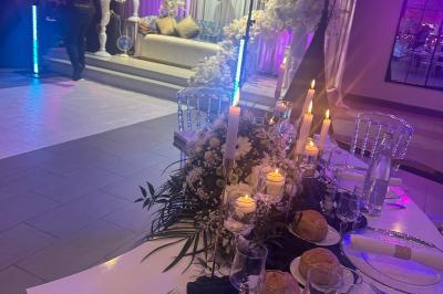 Salle de réception élégante avec tables décorées de fleurs blanches, chaises transparentes et éclairage tamisé.