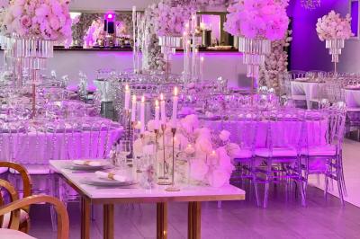 Salle de réception élégante avec tables décorées de fleurs blanches, chaises transparentes et éclairage tamisé.